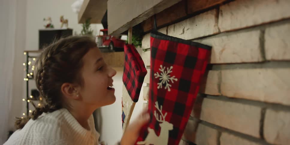 Girl hangs christmas stockings on hooks on mantle