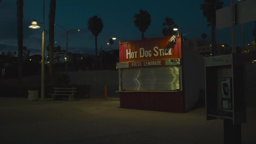 A hot dog stand in a park is boarded up at night