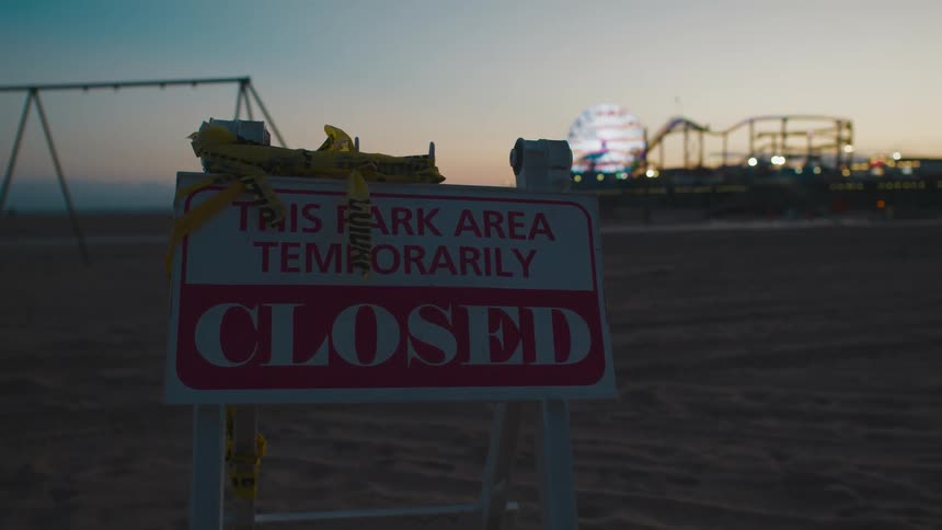 At sunset a brightly illuminated fairground is located near to a small abandoned playground