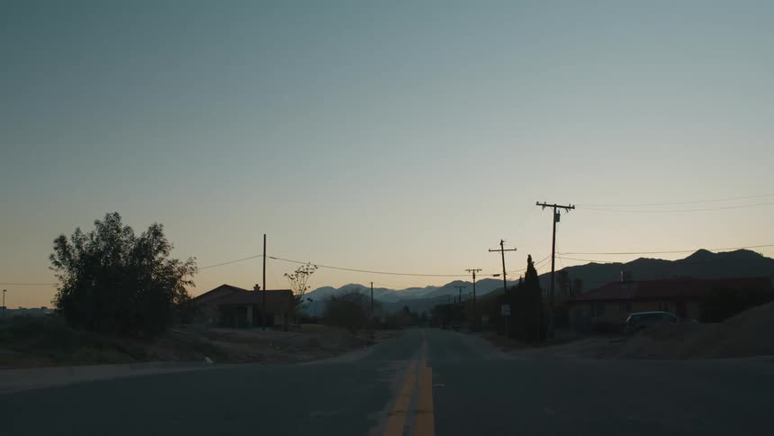 A road with houses trees a mountain range the sky and clouds in the background