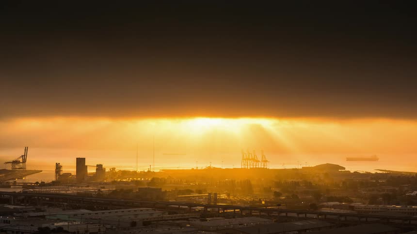 The sun is partially shining through some heavy clouds over a city