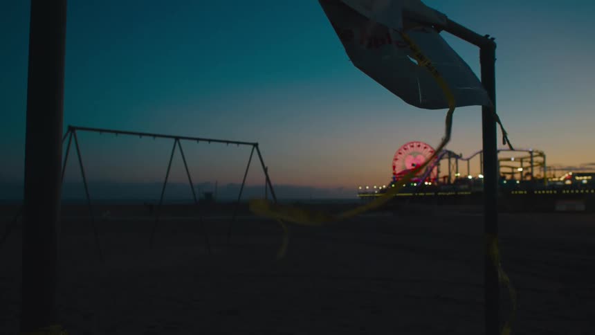 A kite hangs from a metal pole in a playground as a brightly lit fairground is seen in the background