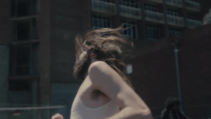 A homeless man with long hair and beard plays air guitar and dances in a homeless camp