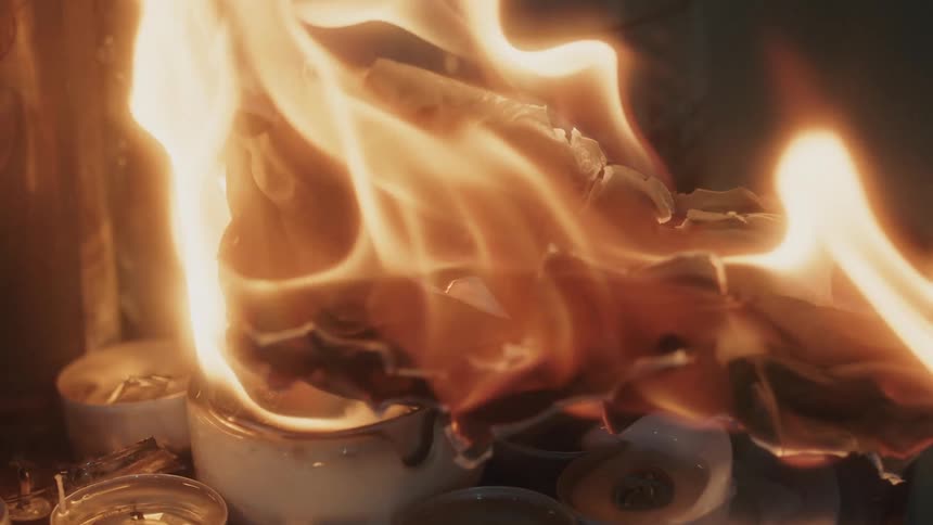 A piece of paper burns in the flame of several candles