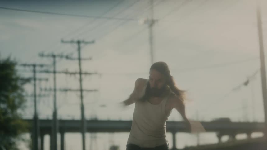 A man dancing with an overpass vehicles the sky and clouds in the background