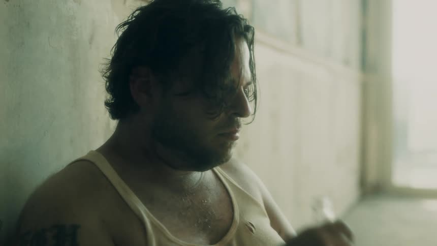 A man on the floor by a wall drinking a bottle of beer
