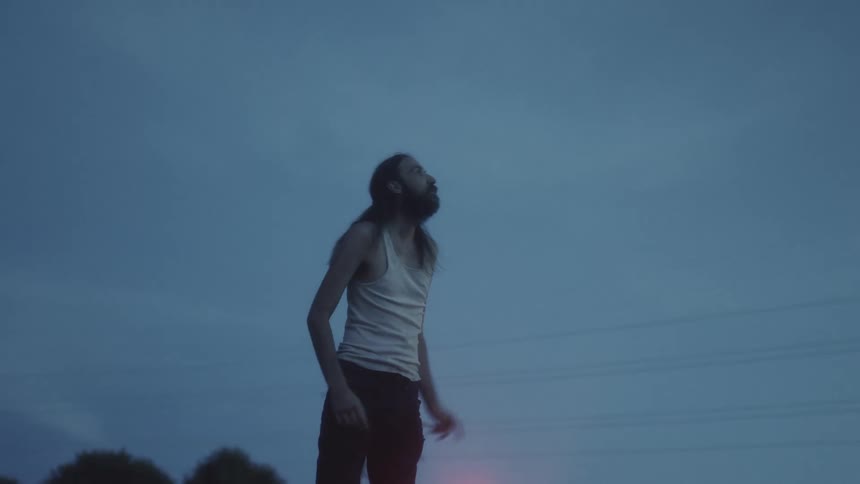 A man stands up in the back of a pickup and triumphantly holds his hands up and shouts