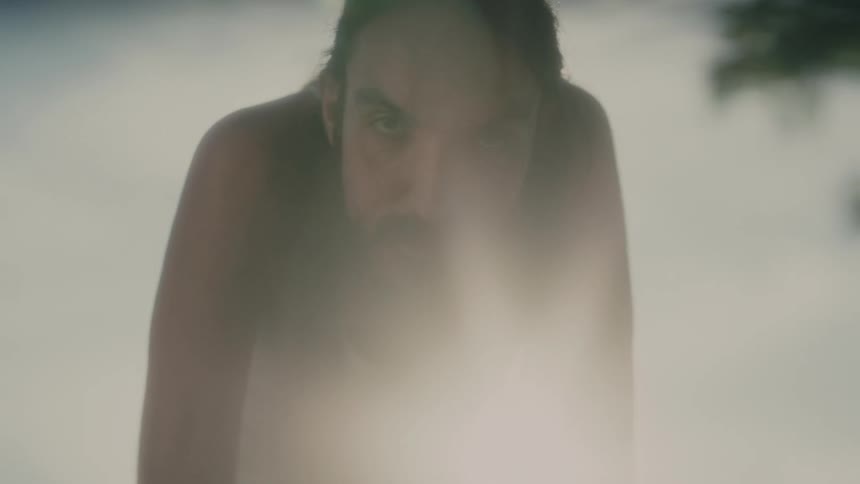 A man bends over to stare into the camera as the sun shines behind him