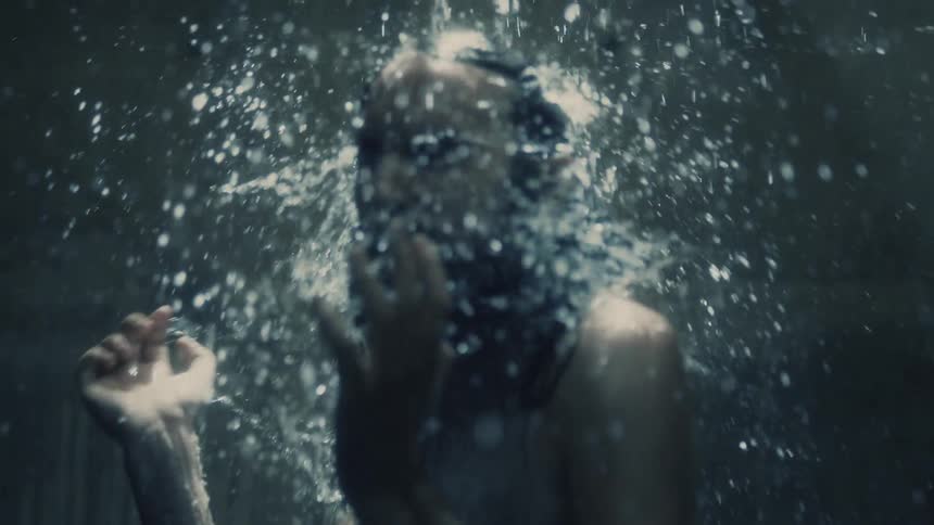 Man stands under shower stroking face then shaking hair