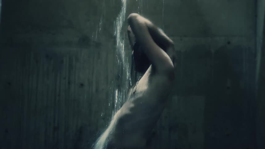 A shirtless man with long hair and beard sways as he washes himself with water pouring down from above