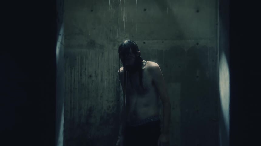 Man stands bare chested in dimly lit room as water falls from above