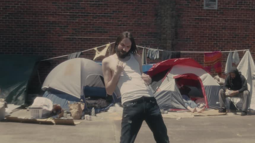 Man plays air guitar standing near tents and clothes lines near brick wall