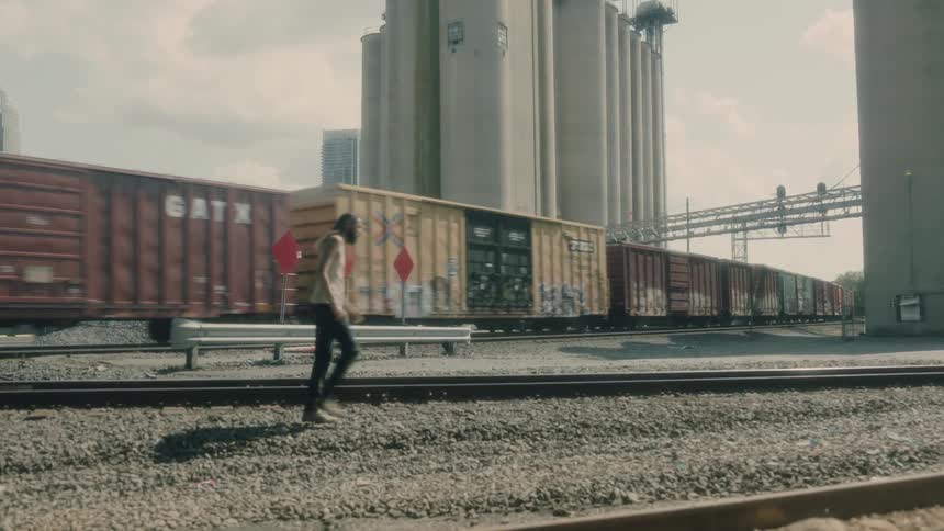 A man walking near railroad tracks with a train traveling in the background