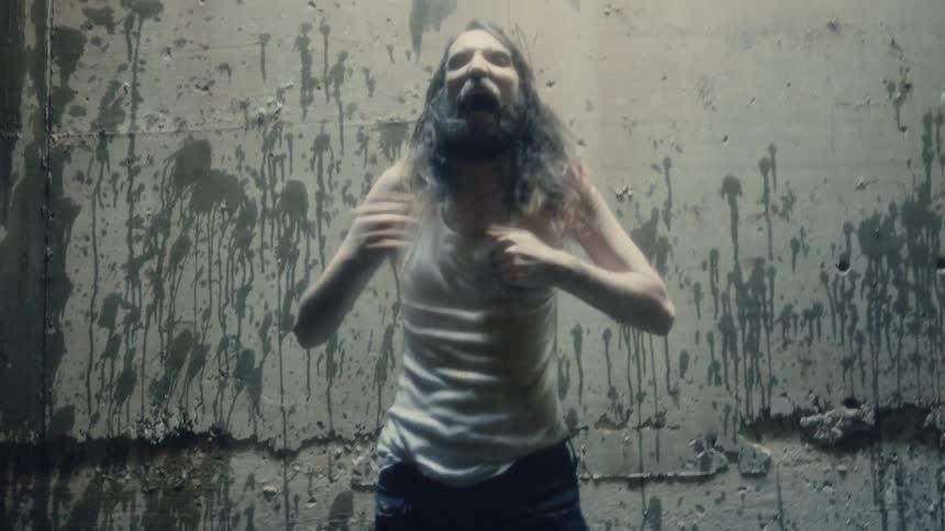 A man in a room beating his chest when a wall in the background