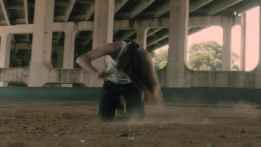 Man on kneeling on dirt under underpass swipes ground and slams hands down as vehicle passes