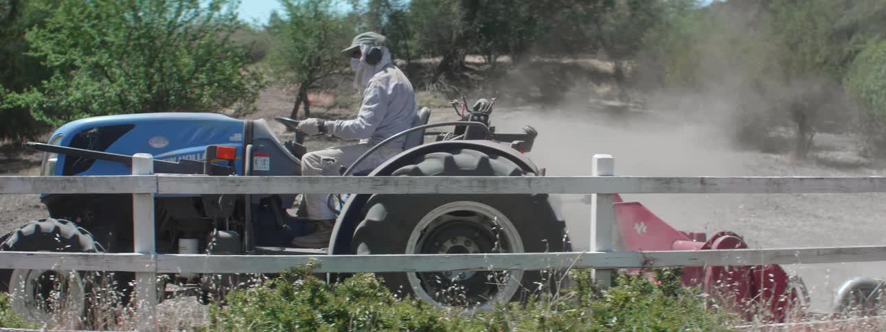 A farmer plowing a dirt field with a tractor on a sunny day