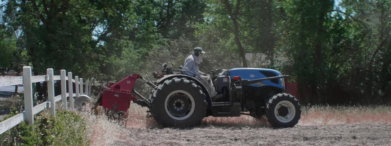 A farmer kicking up dust while plowing a dirt field