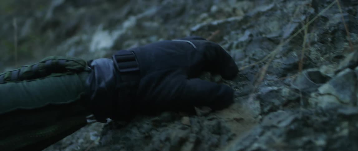 A man wearing thick padded gloves climbs up the side of a muddy hill