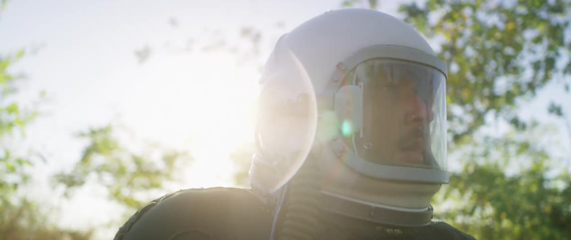 A scared man in a helmet walking through trees on a sunny day