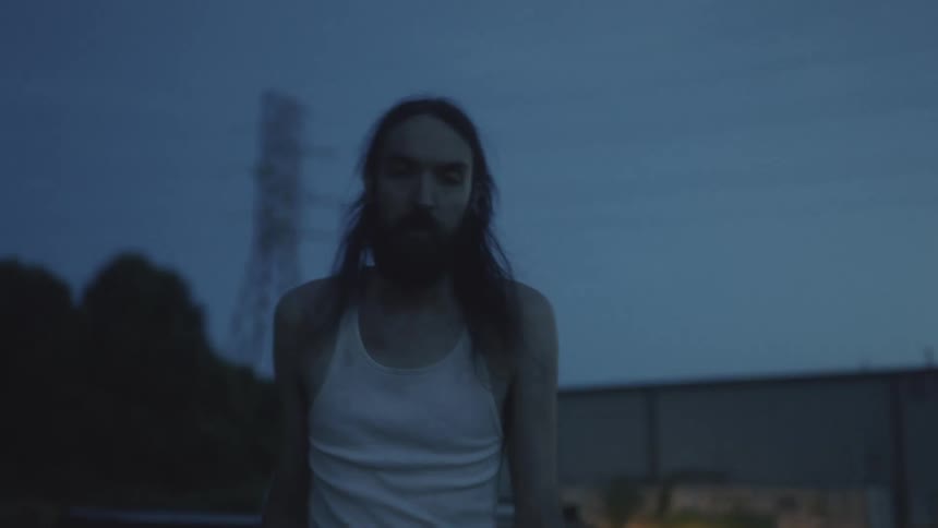 A man climbs out of the back of a truck and approaches the camera as the truck drives away in the evening