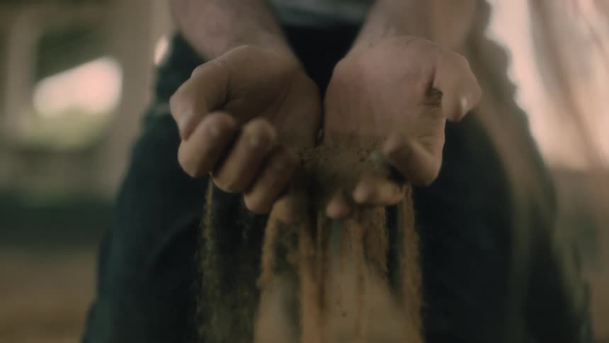 A kneeling man allows dirt to sift and fall through his open hands