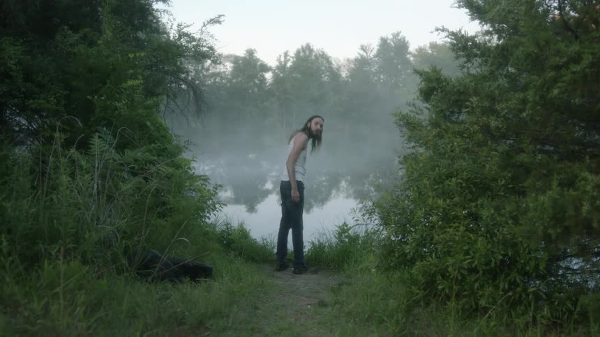A man stands on the shore of a lake and looks around