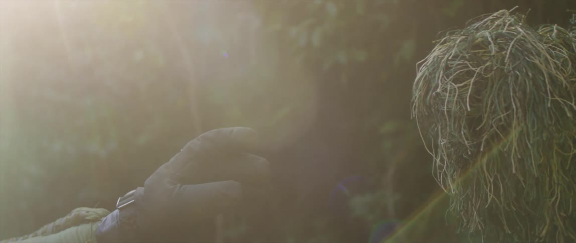 A gloved hand reaches out slowly to touch a grass covered arm