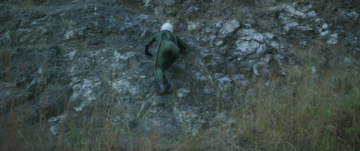 A person with a helmet and a flight suit trying to climb up a hill