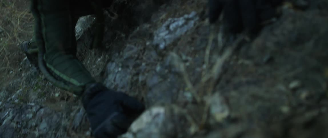 A man in an astronaut suit struggles to climb up a steep slope covered in loose rocks and dirt