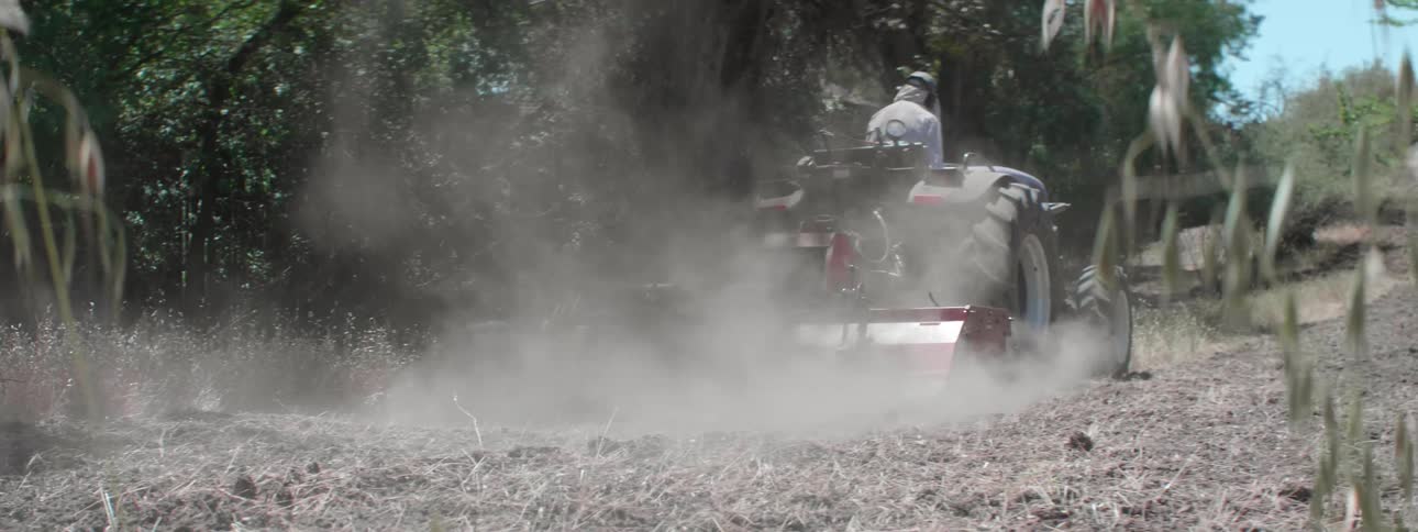A farmer plowing a dirt field with a tractor on a sunnyd ay