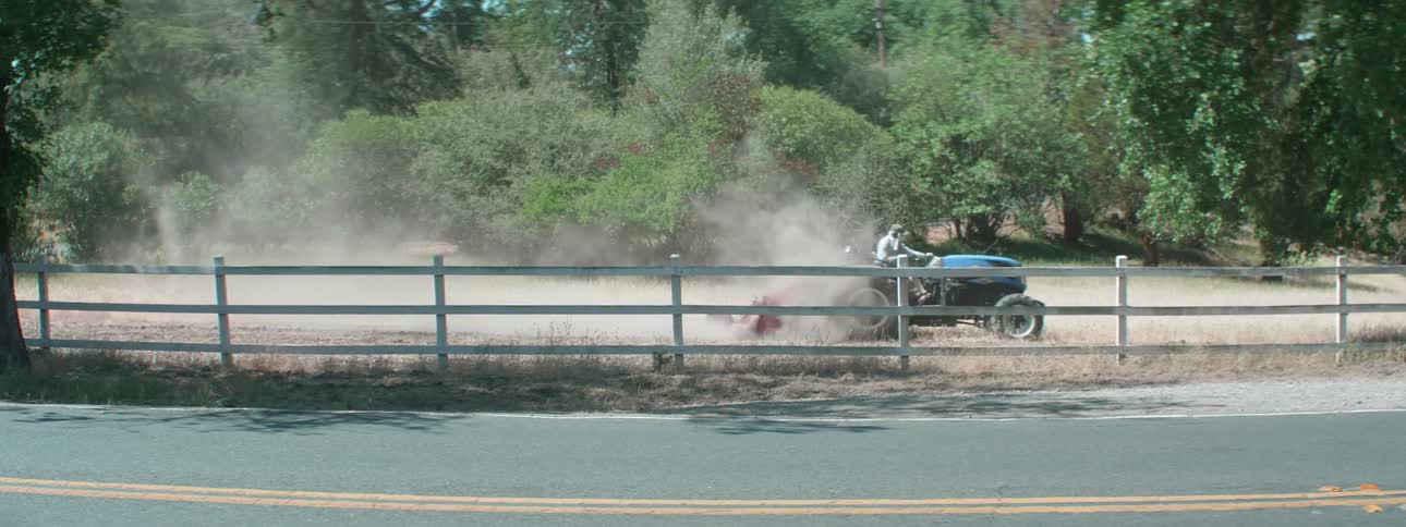A farmer drives a tractor turning over the soil kicking up dust
