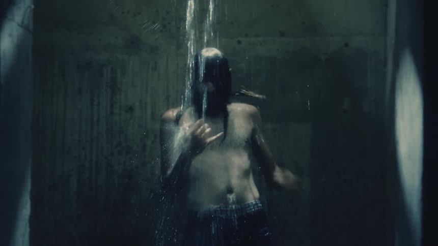 A man in a room shaking with water falling on him with a wall in the background