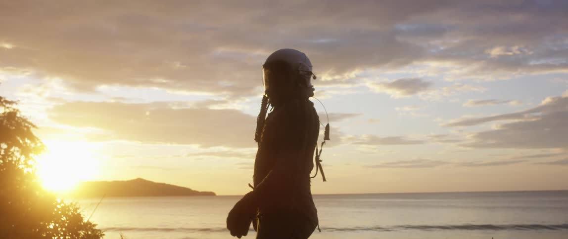 A man in a helmet runs toward the ocean and stops to look around