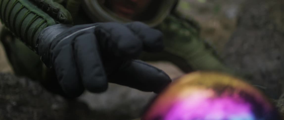 A man in a helmet and green suit reaches out for a rainbow colored ball while straddling on rocks