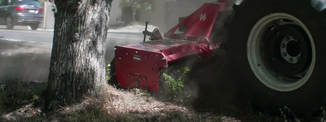 A person drives a tractor that is dragging an apparatus that is turning the dry soil