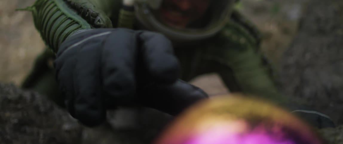 A person is reaching for an object on the ground and wearing a helmet