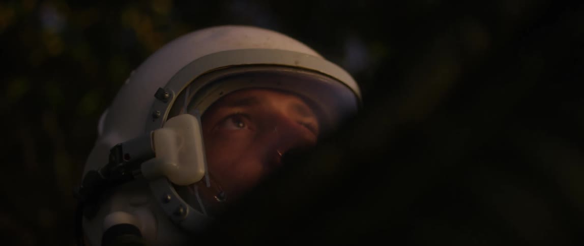 A male astronaut points a device outward as he surveys his surroundings