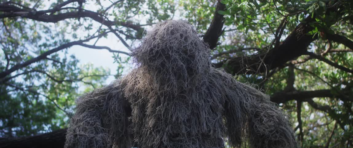 A man is wearing camouflage outdoors in a forest