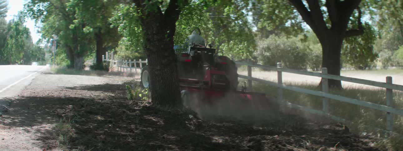 A man drives a tractor through the soil on the side of a road on a sunny day
