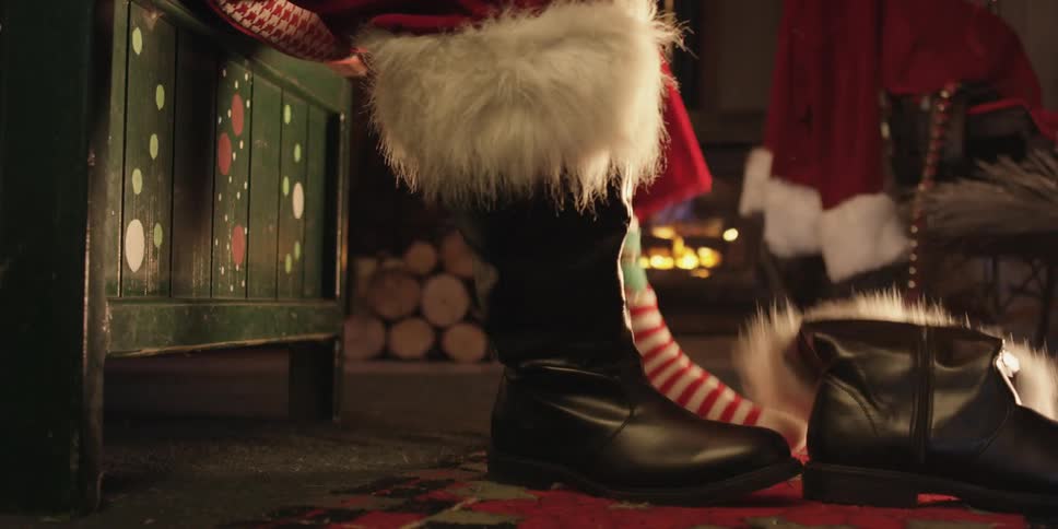A person dressed as santa claus taking off a fur lined boot next to a fireplace