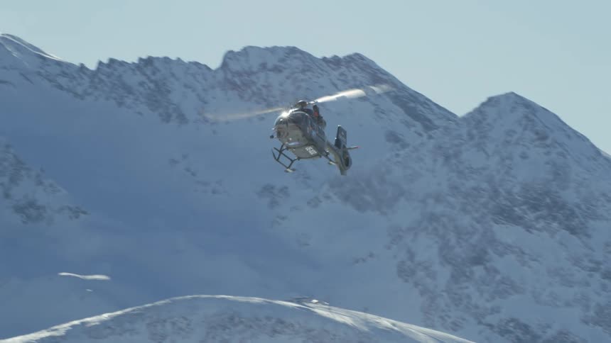 A helicopter flying with a snow covered mountain range the sky and clouds in the background