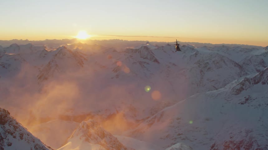 A helicopter flying over a snowy mountain range at sunset