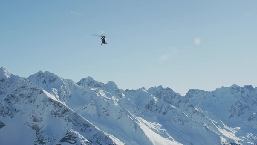 A helicopter flies over a mountain range covered in a thick blanket of snow