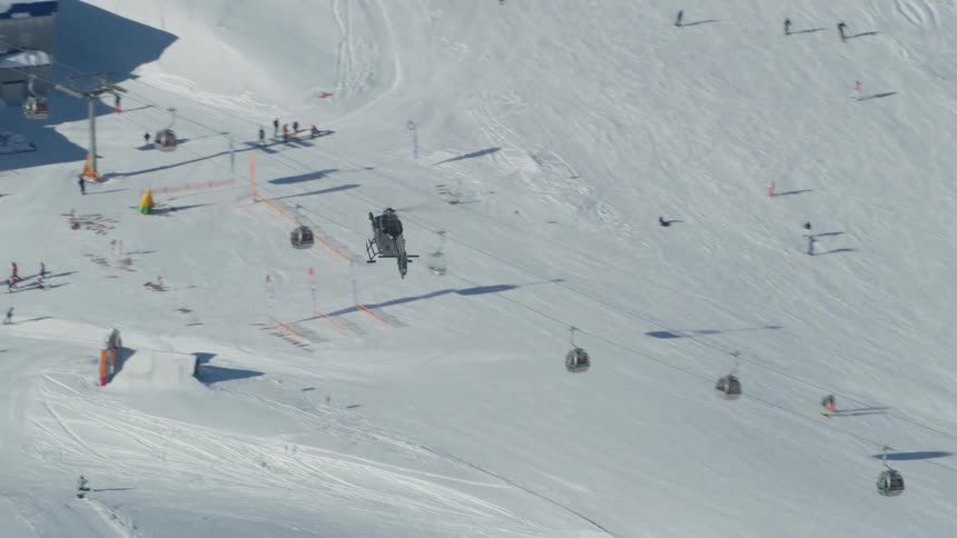 A helicopter flying over a snowy slope with people skiing and buildings
