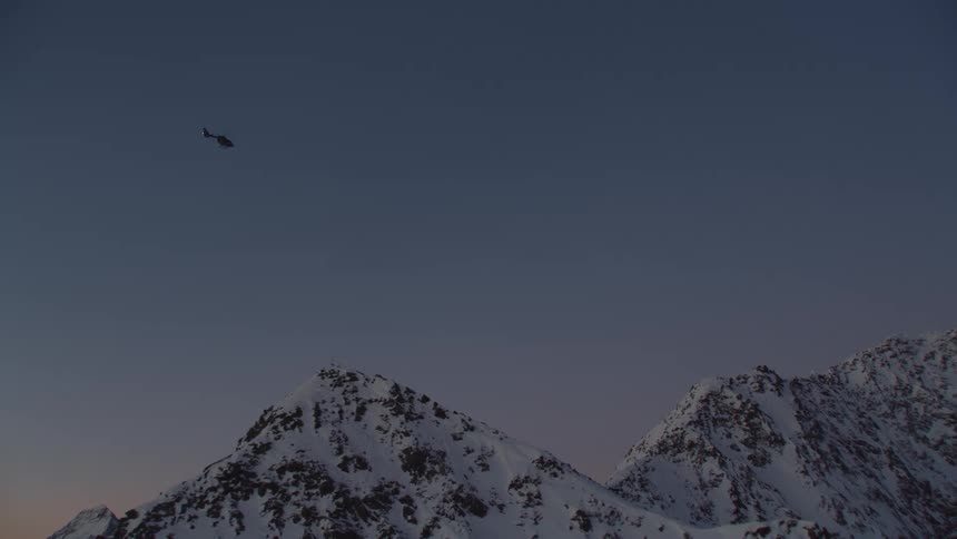 A helicopter flying over a snowy mountain range in winter