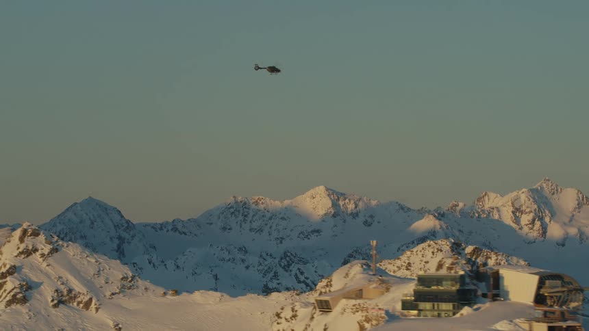 A helicopter flying over a snowy mountain range at dawn