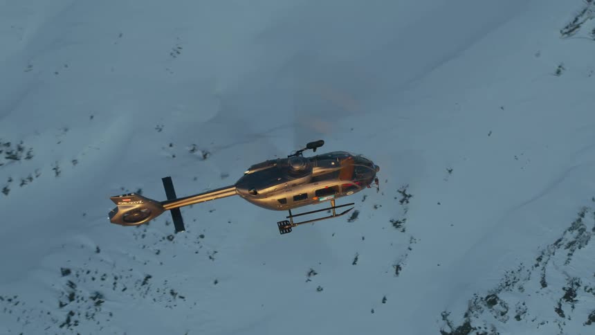 A helicopter hovers above a snow covered rocky slope