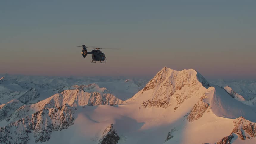 A helicopter is flying above a mountain range covered in snow