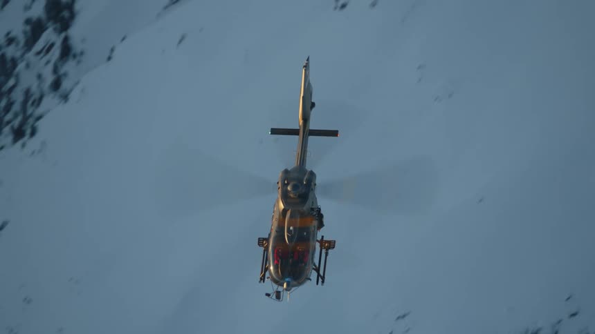 A helicopter flies above a snow covered rocky slope