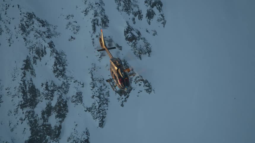 A helicopter flying over a snowy mountain range in winter
